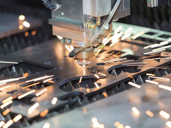 Une machine de découpe laser en action, produisant des étincelles lors de la découpe d'une pièce métallique.