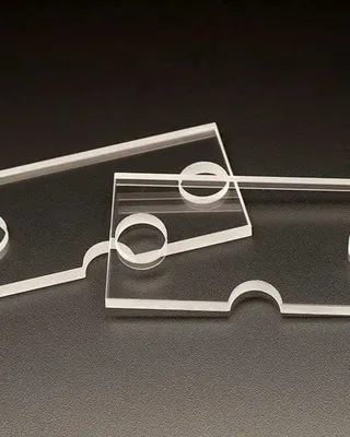 Deux pièces de plastique transparent en forme de rectangles avec une moitié ronde découpée, posées sur une surface sombre.