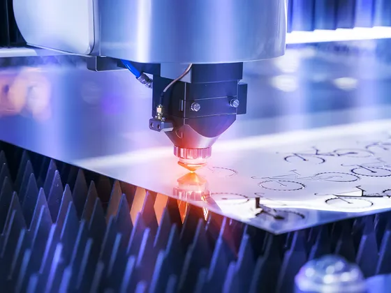 Une machine de découpe laser en action, coupant une feuille de métal avec des motifs circulaires, dans un environnement industriel.