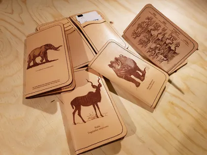 Set de cartes en cuir illustrant des animaux préhistoriques avec noms et descriptions, disposées sur une surface en bois.