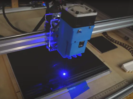 Une machine de gravure laser en action, utilisant une diode laser bleue pour graver sur une plaque noire posé sur une surface en bois.