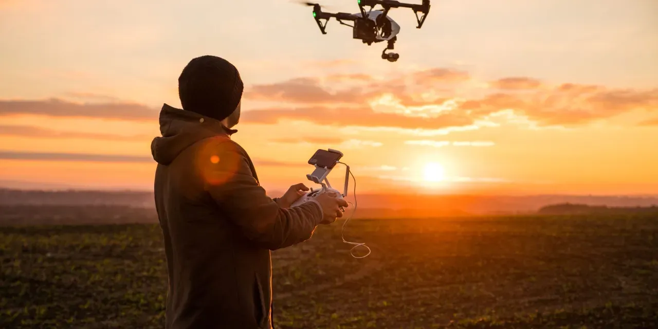 homme pilotant un drone en plein couché du soleil