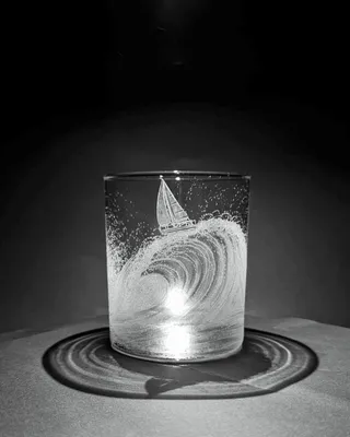 Verre en verre avec une gravure d'une vague et d'un voilier, éclairé pour créer l'effet d'une vague et une ombre circulaire.
