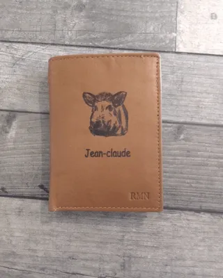Pochette en cuir marron clair avec un tache de tigre noir et manuel inscrit "Jean-Claude" et les initials "RMN" en bas à droite.