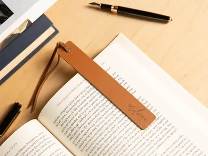 Livre ouvert avec marque-page en cuir marron avec une inscription en cursive, stylo à bille noir et or, et autres documents sur un bureau en bois.