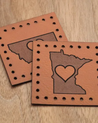 Deux tampons en cuir, chacun représentant une carte de l'État du Minnesota avec un cœur au centre, posés sur une surface en bois.