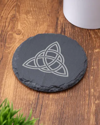 Plaque ronde en ardoise noire avec un motif celtique en forme de nœud, placé sur une table en bois.