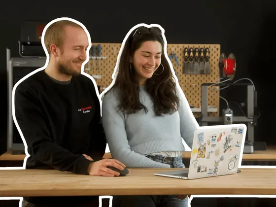 Deux jeunes femmes regardent un ordinateur portable décoré de stickers, dans un atelier ou un espace de travail, avec des outils en arrière-plan.