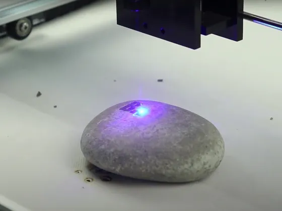 Une roche grise sur une surface blanche avec un laser violet pointé dessus, un appareil automatisé au-dessus