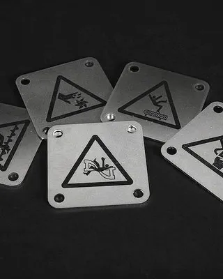 Six plaques métalliques avec des symboles d'avertissement, posées sur une surface sombre.