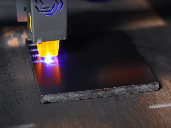 Une machine de découpe laser en action, coupant une plaque de matériau noir sur une surface en bois.
