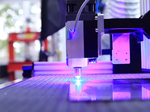 Une machine de fabrication de circuits imprimés avec un laser violet sur une plaque métallique.