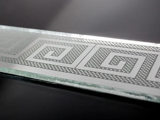 Détail d'une plaque en verre avec un motif géométrique en spirale, encadré par un contour à motifs en losange.