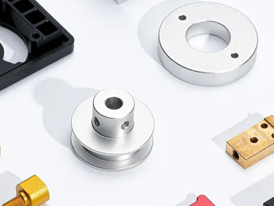 Différents composants mécaniques en métal et plastique sur une surface blanche, incluant des pièces en cuivre, en acier et en plastique noir.