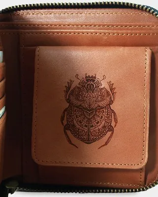 Un porte-monnaie en cuir marron avec une illustration d'insecte gravée sur une poche