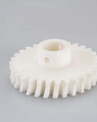 Une pièce en plastique blanc, probablement une roue dentée, avec des dents et un trou central.