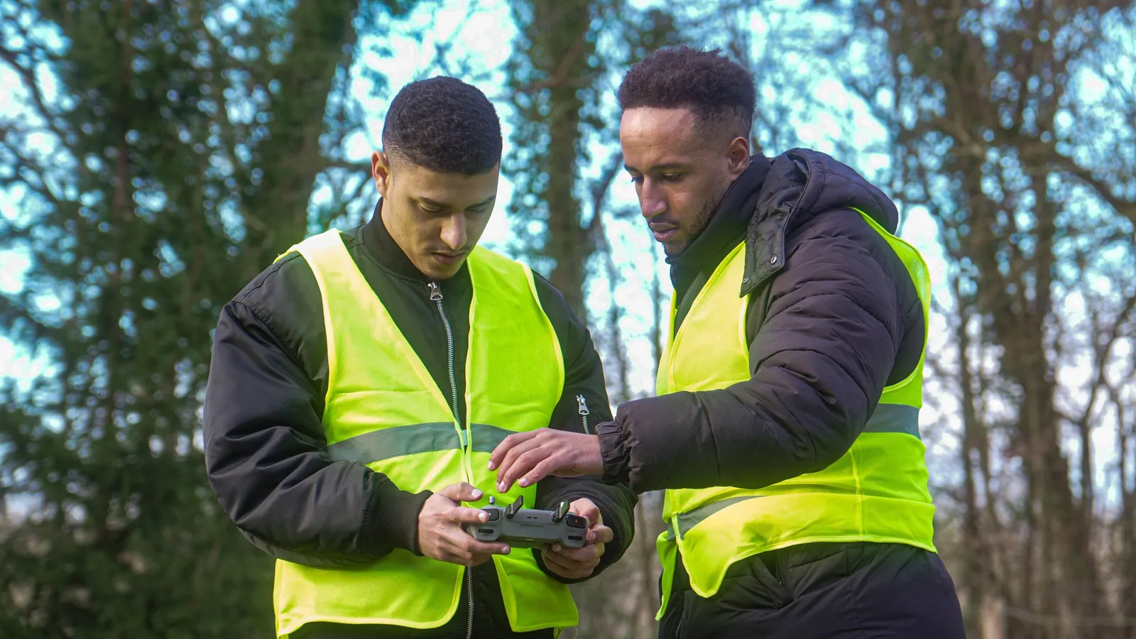 Deux télépilotes en gilet de sécurité observant un drone en forêt