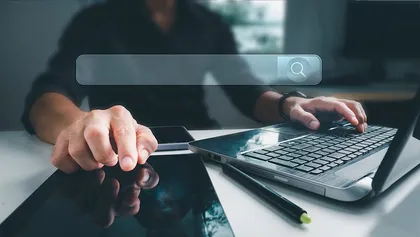 Personne utilisant un ordinateur portable et une tablette, avec une barre de recherche virtuelle flotte au-dessus de la tablette.