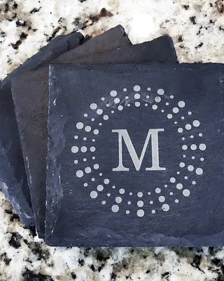 Dessus de tuiles en ardoise gravé avec un cercle de points et la lettre M au centre, posé sur un plan de travail en granite.
